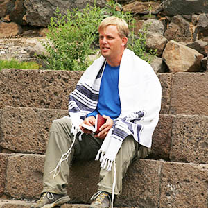 Todd Lanting sitting on stone steps in Israel wearing a traditional Tallit prayer shawl.